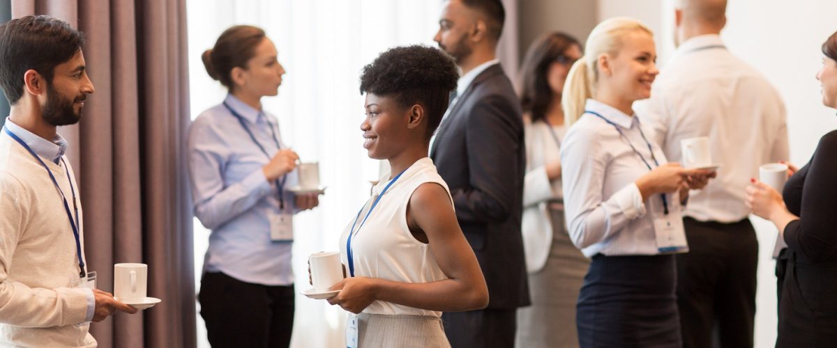 business and education concept - international group of people with conference badges drinking coffee
